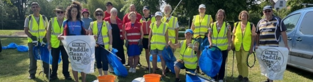 A group of people in hi-viz vests stand behind two paddle board and a kayak