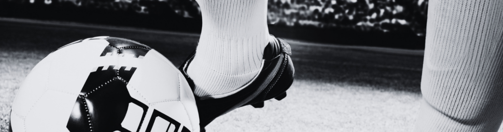 Black and white close up of a person's football boot on top of a football