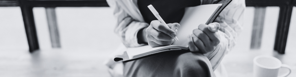 Person writing in a notebook with a pen.